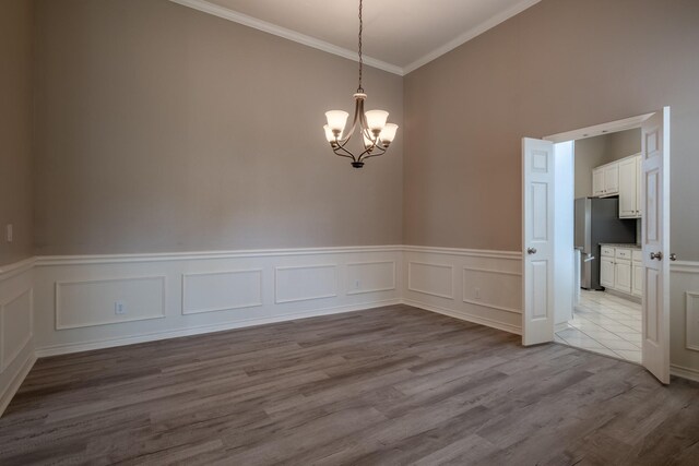 spare room with ornamental molding, a towering ceiling, light wood-type flooring, and a chandelier