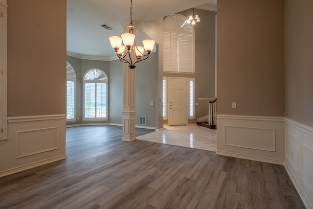 unfurnished dining area featuring an inviting chandelier, decorative columns, crown molding, and hardwood / wood-style floors