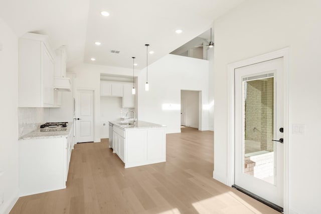 kitchen featuring decorative backsplash, light wood-type flooring, an island with sink, decorative light fixtures, and white cabinetry