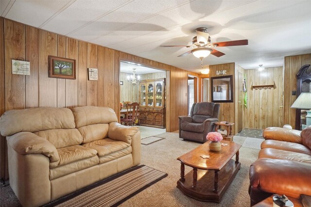 carpeted living room featuring wood walls and ceiling fan with notable chandelier