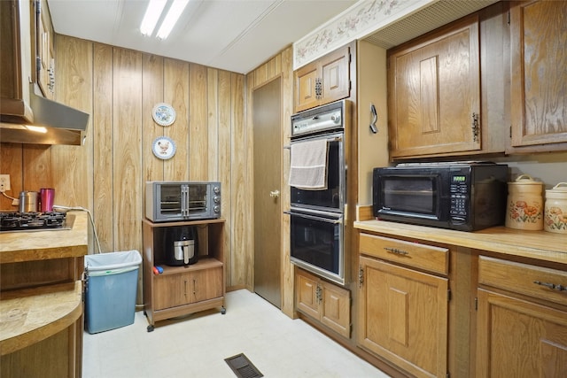 kitchen with appliances with stainless steel finishes, wood walls, wall chimney exhaust hood, and light tile patterned floors