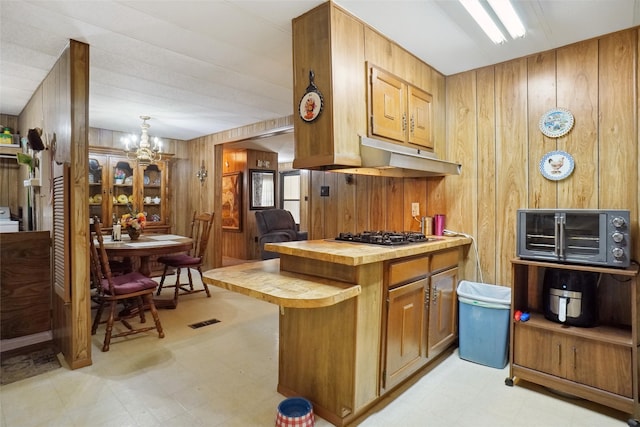 kitchen with a notable chandelier, wood walls, gas stovetop, and light tile patterned floors