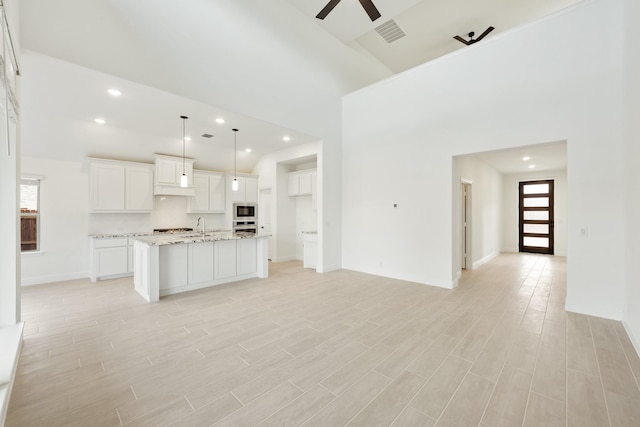 unfurnished living room with a high ceiling, ceiling fan, and light wood-type flooring