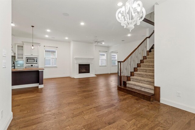 unfurnished living room with ceiling fan with notable chandelier and wood-type flooring