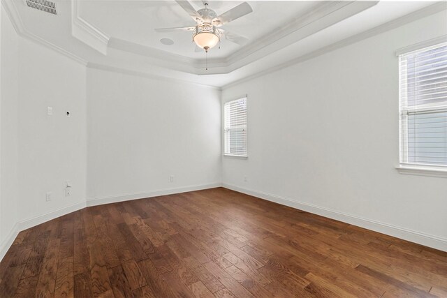 unfurnished room featuring a healthy amount of sunlight, ceiling fan, a raised ceiling, and hardwood / wood-style floors