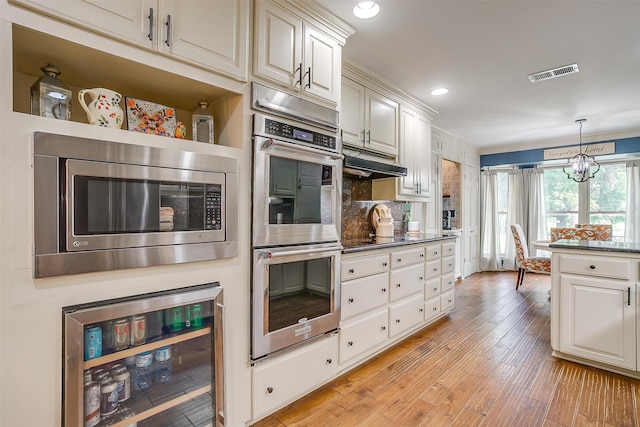 kitchen with a chandelier, hanging light fixtures, stainless steel appliances, wine cooler, and light hardwood / wood-style flooring