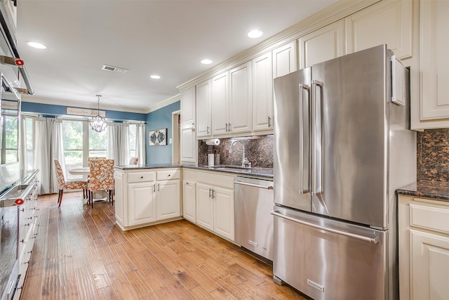 kitchen featuring tasteful backsplash, stainless steel appliances, pendant lighting, kitchen peninsula, and light wood-type flooring