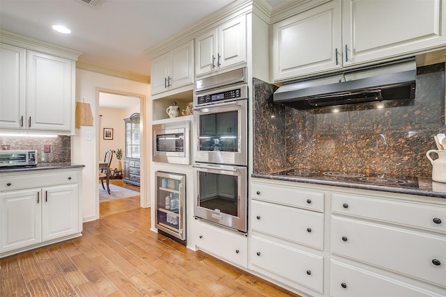 kitchen featuring decorative backsplash, ornamental molding, dark stone countertops, appliances with stainless steel finishes, and light hardwood / wood-style flooring