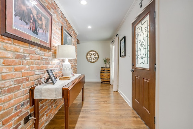 foyer entrance with light hardwood / wood-style floors, ornamental molding, and brick wall