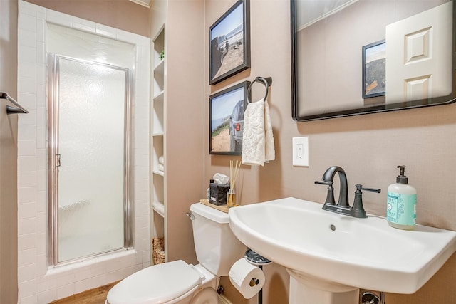 bathroom featuring a shower with shower door, built in features, toilet, and sink