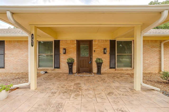 property entrance with brick siding, roof with shingles, and a porch