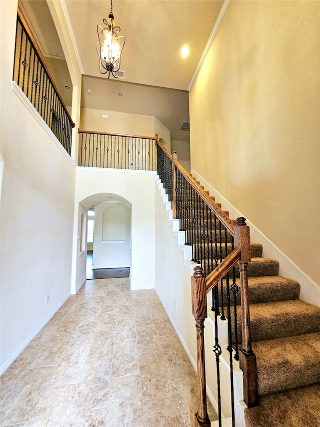 stairway featuring a towering ceiling, tile patterned floors, crown molding, and a notable chandelier