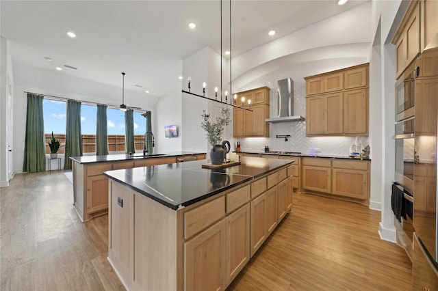 kitchen with kitchen peninsula, hanging light fixtures, decorative backsplash, light wood-type flooring, and wall chimney exhaust hood