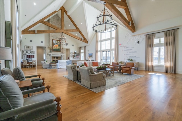 living room with a fireplace, high vaulted ceiling, beamed ceiling, an inviting chandelier, and light hardwood / wood-style floors