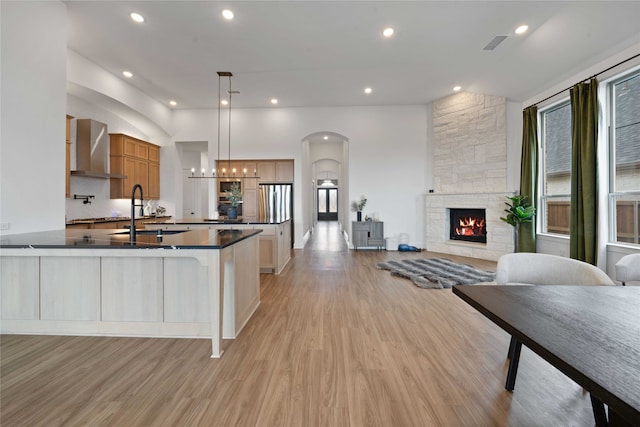 kitchen with sink, light hardwood / wood-style flooring, a stone fireplace, and wall chimney exhaust hood