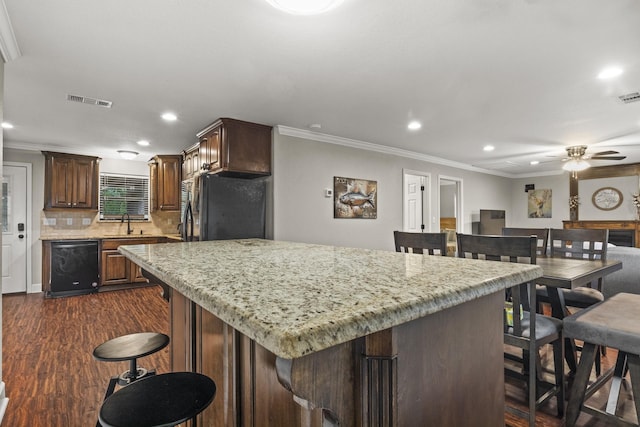 kitchen featuring light stone counters, ornamental molding, a kitchen island, decorative backsplash, and black appliances