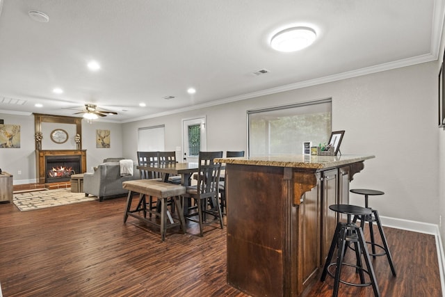 interior space featuring a kitchen bar, ornamental molding, a center island, ceiling fan, and dark wood-type flooring