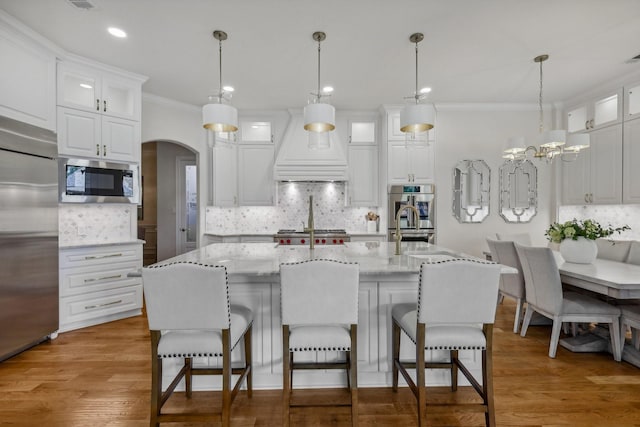 kitchen with white cabinetry, stainless steel appliances, a kitchen island with sink, and custom exhaust hood