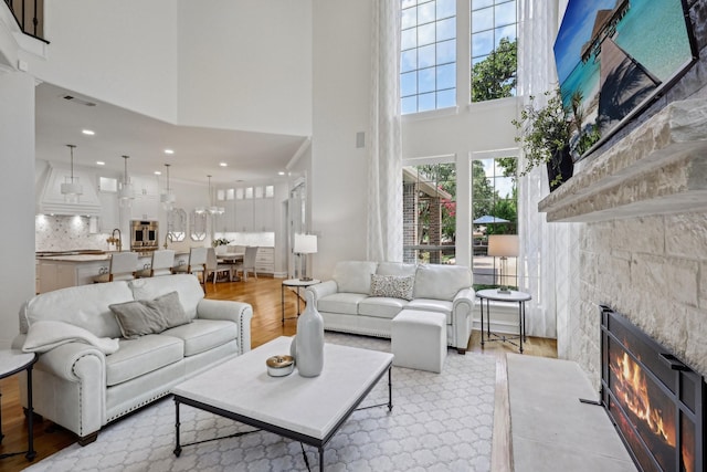 living room featuring a tiled fireplace, sink, a towering ceiling, and light hardwood / wood-style flooring