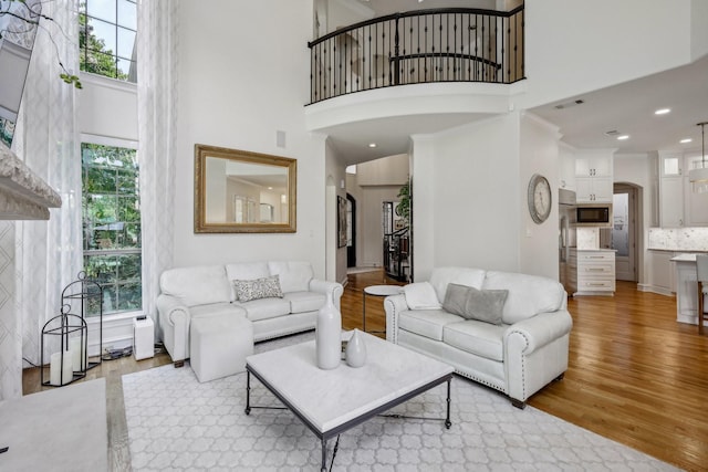 living room featuring a high ceiling, a wealth of natural light, and light hardwood / wood-style flooring