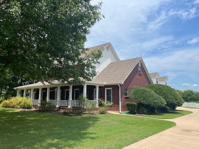 view of front facade with brick siding, covered porch, and a front yard