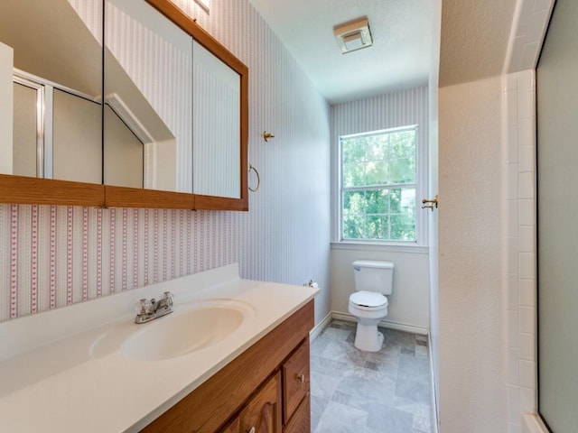 bathroom with toilet, wallpapered walls, vanity, and a shower with shower door