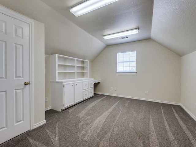 bonus room featuring dark carpet, a textured ceiling, and lofted ceiling