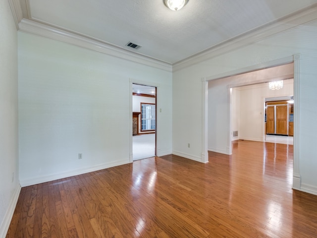 empty room with visible vents, wood-type flooring, baseboards, and ornamental molding