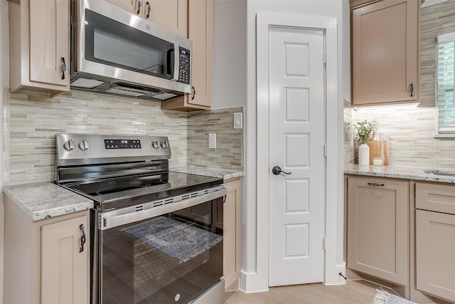 kitchen with light hardwood / wood-style flooring, backsplash, light stone countertops, appliances with stainless steel finishes, and light brown cabinetry