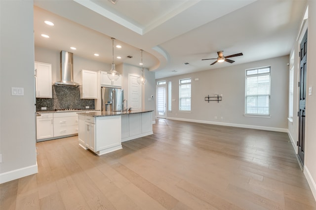 kitchen featuring light wood-type flooring, stainless steel refrigerator with ice dispenser, wall chimney exhaust hood, and a center island with sink