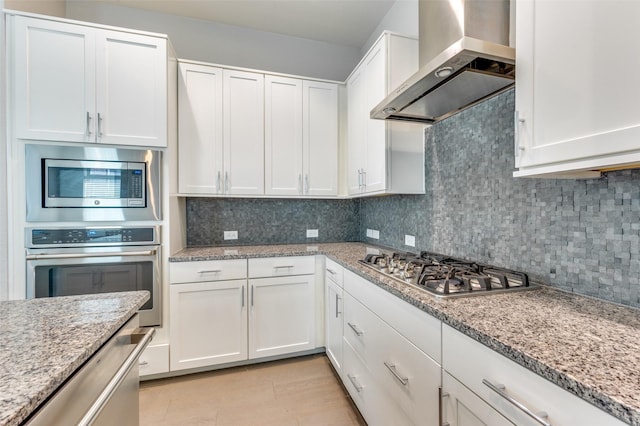 kitchen featuring wall chimney exhaust hood, decorative backsplash, white cabinets, and appliances with stainless steel finishes