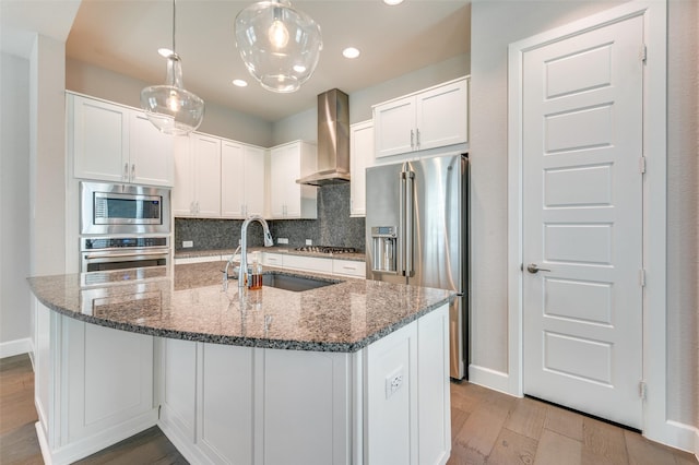 kitchen with backsplash, sink, appliances with stainless steel finishes, wall chimney exhaust hood, and light hardwood / wood-style floors