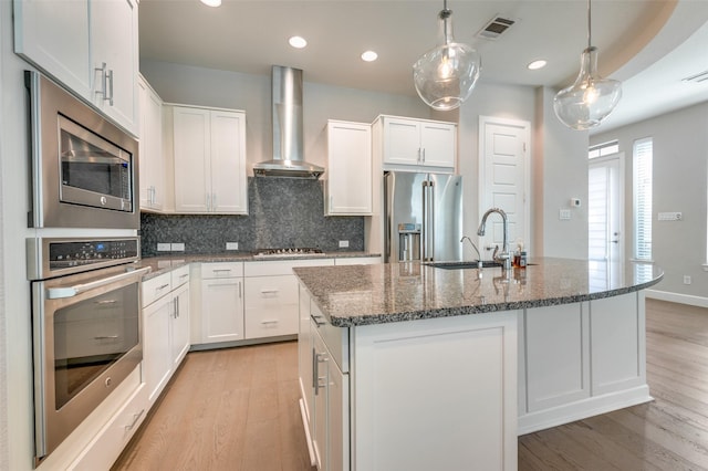 kitchen featuring wall chimney range hood, light wood-type flooring, white cabinets, and stainless steel appliances