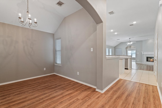 empty room featuring a tile fireplace, ceiling fan with notable chandelier, light hardwood / wood-style flooring, and vaulted ceiling