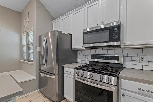 kitchen with appliances with stainless steel finishes, vaulted ceiling, light tile patterned floors, decorative backsplash, and white cabinetry