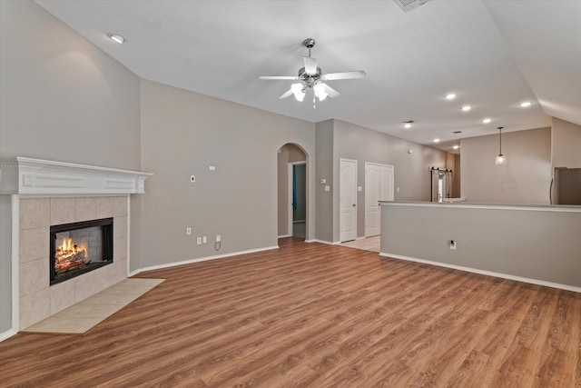 unfurnished living room featuring a tile fireplace, vaulted ceiling, light hardwood / wood-style flooring, and ceiling fan