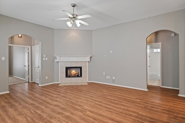 unfurnished living room featuring wood-type flooring, a tiled fireplace, and ceiling fan