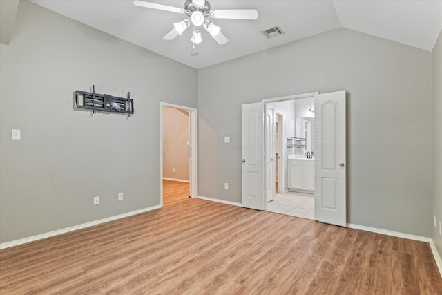 unfurnished bedroom featuring connected bathroom, lofted ceiling, light tile patterned floors, and ceiling fan