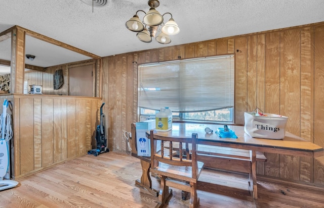 dining room with a notable chandelier, a textured ceiling, wooden walls, and light hardwood / wood-style flooring