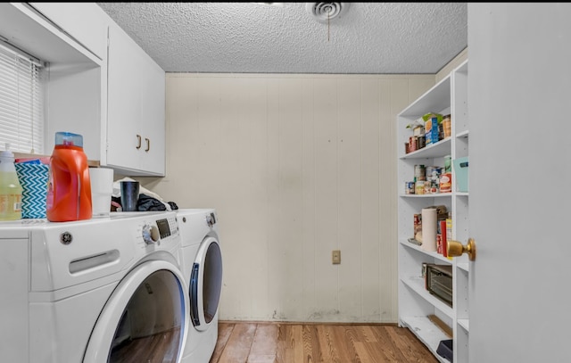 laundry area featuring cabinets, light hardwood / wood-style flooring, independent washer and dryer, a textured ceiling, and wooden walls