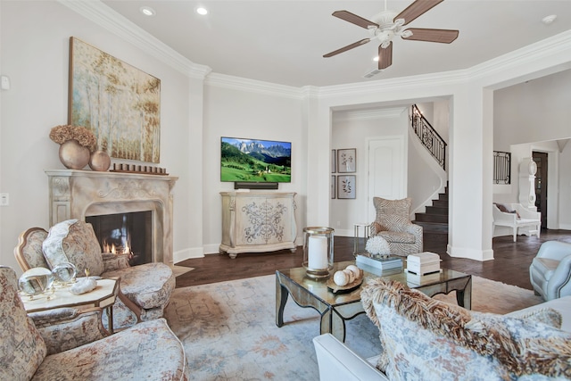 living room with wood-type flooring, ceiling fan, crown molding, and a high end fireplace