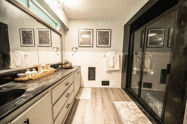 bathroom with a shower with shower door, tile walls, hardwood / wood-style flooring, and double sink vanity