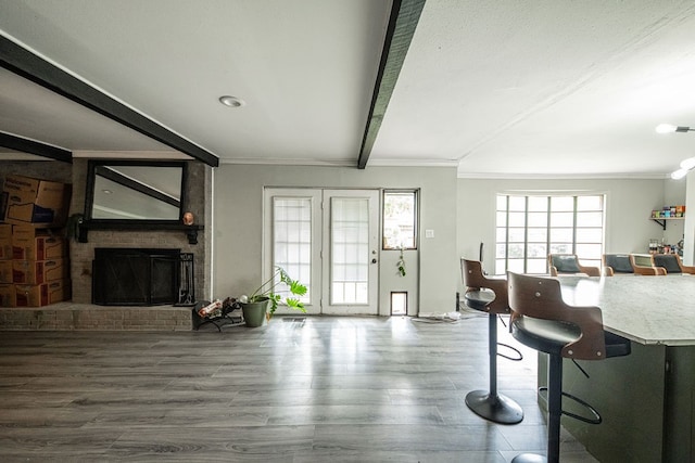 living room with hardwood / wood-style flooring, beamed ceiling, a brick fireplace, and ornamental molding