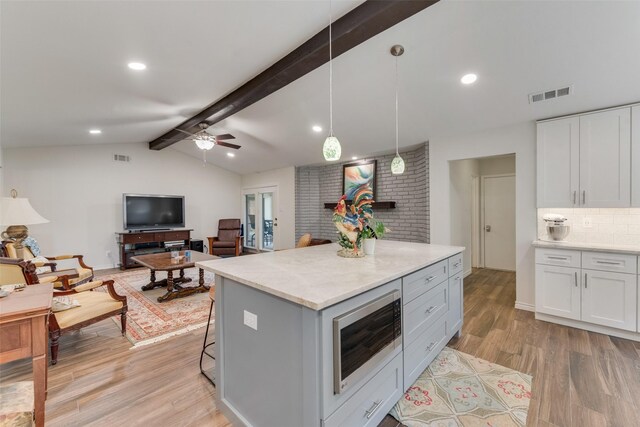 kitchen featuring built in microwave, a breakfast bar, white cabinetry, hanging light fixtures, and light hardwood / wood-style flooring