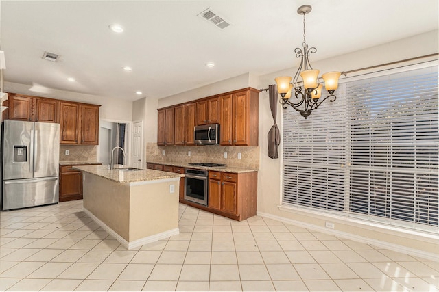 kitchen with pendant lighting, appliances with stainless steel finishes, sink, light stone countertops, and a center island with sink