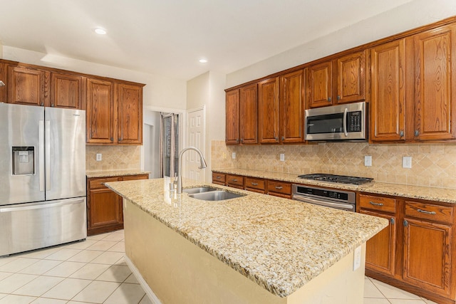 kitchen with light stone countertops, a kitchen island with sink, light tile patterned floors, sink, and stainless steel appliances