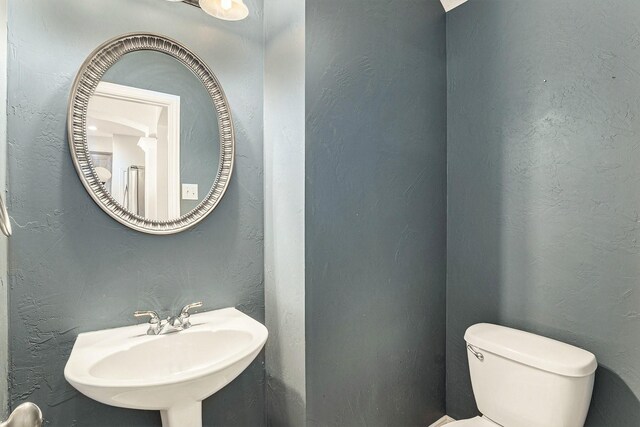 bathroom with toilet, a textured wall, and a sink