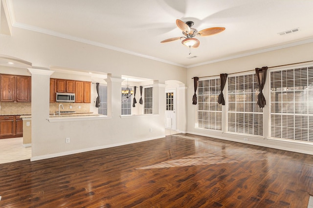 unfurnished living room with decorative columns, ceiling fan with notable chandelier, crown molding, and hardwood / wood-style floors