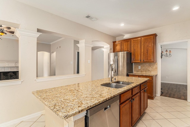 kitchen featuring appliances with stainless steel finishes, sink, light stone countertops, a center island with sink, and decorative columns