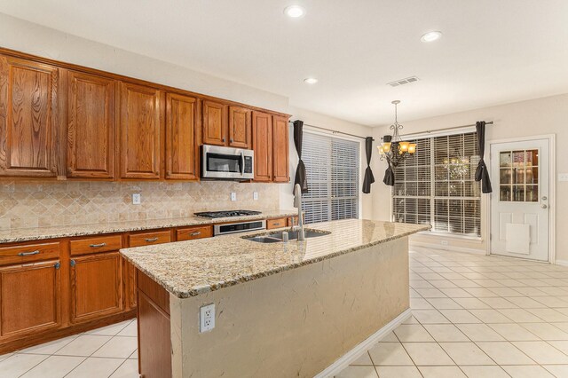 kitchen with light stone countertops, sink, backsplash, stainless steel appliances, and a center island with sink